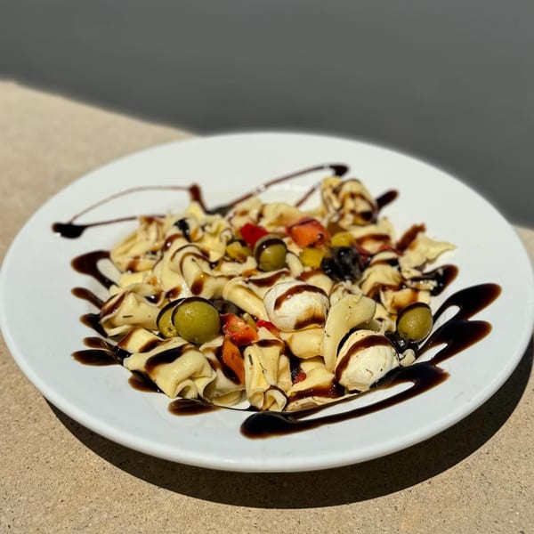 Tortellini pasta salad with olives, mozzarella, and balsamic glaze on a white plate.