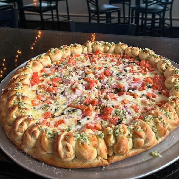Jack's Slice pizza with tomatoes, red onions, and a garlic knot crust on a metal pan.