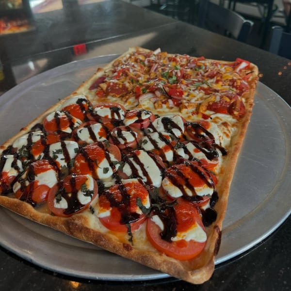 Two rectangular pizzas, one Caprese and one with various toppings, on a metal tray at Jack's Slice.