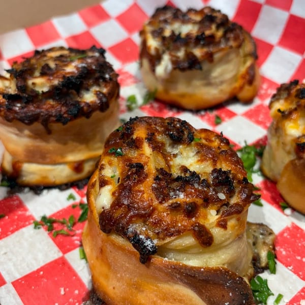 Close-up of several golden-brown pizza rolls with melted cheese and herbs on a red and white checkered paper.