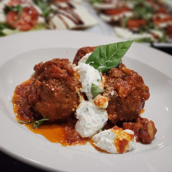 Meatballs in red sauce with dollops of ricotta cheese and fresh basil on a white plate.